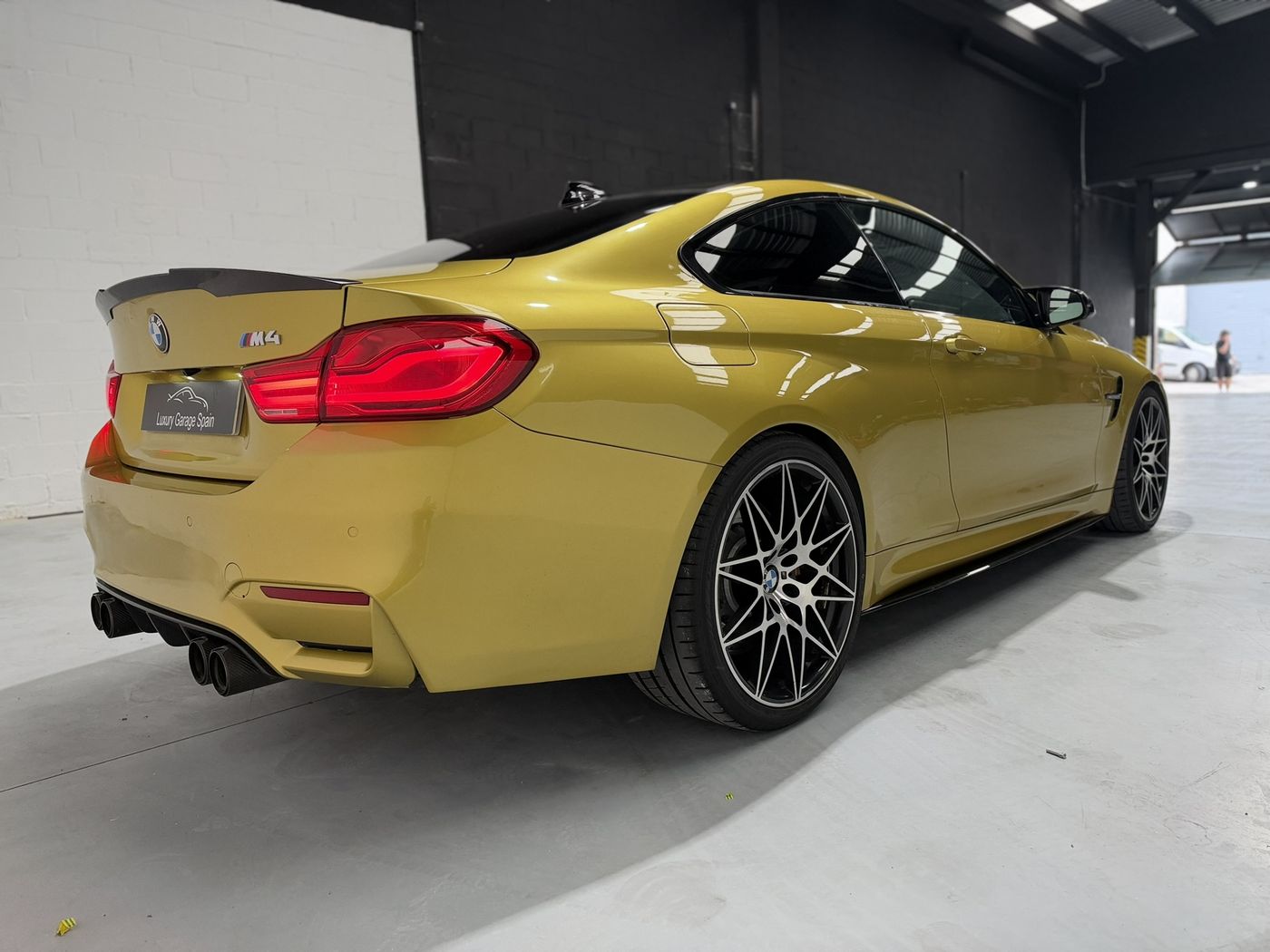 BMW M4 amarillo en tres cuartos traseros, con alerón y cuatro salidas de escape